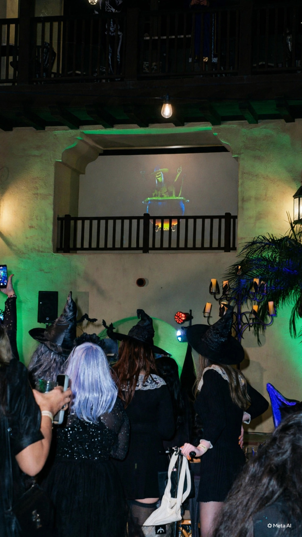 Costumed guests beneath a projected witch and green lighting in Estancia La Jolla's courtyard.