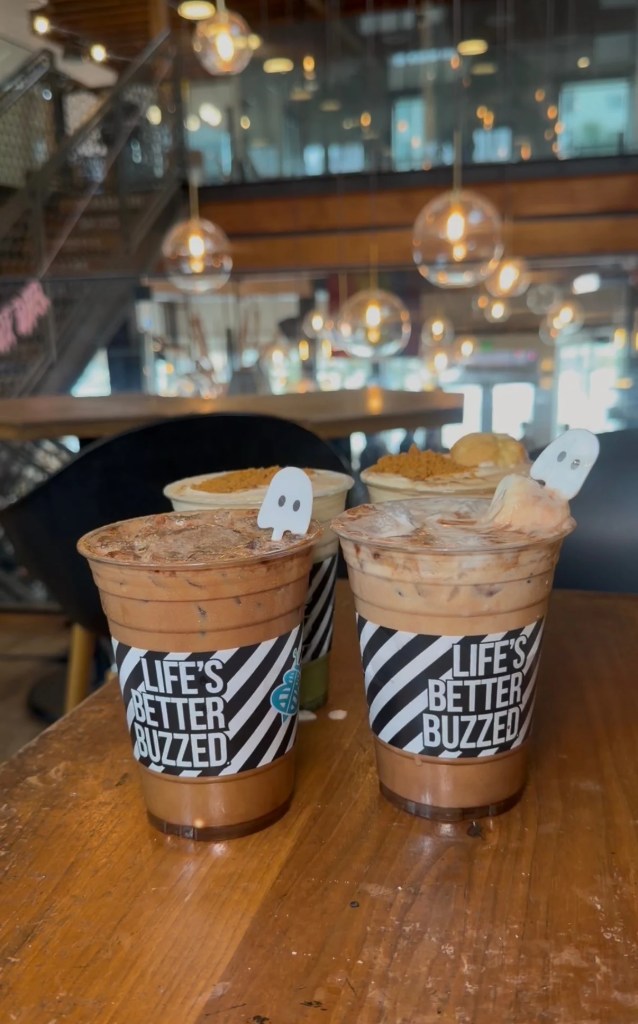 Four Better Buzz iced drinks on a wooden cafe table, with ghost decorations on the two front cups.