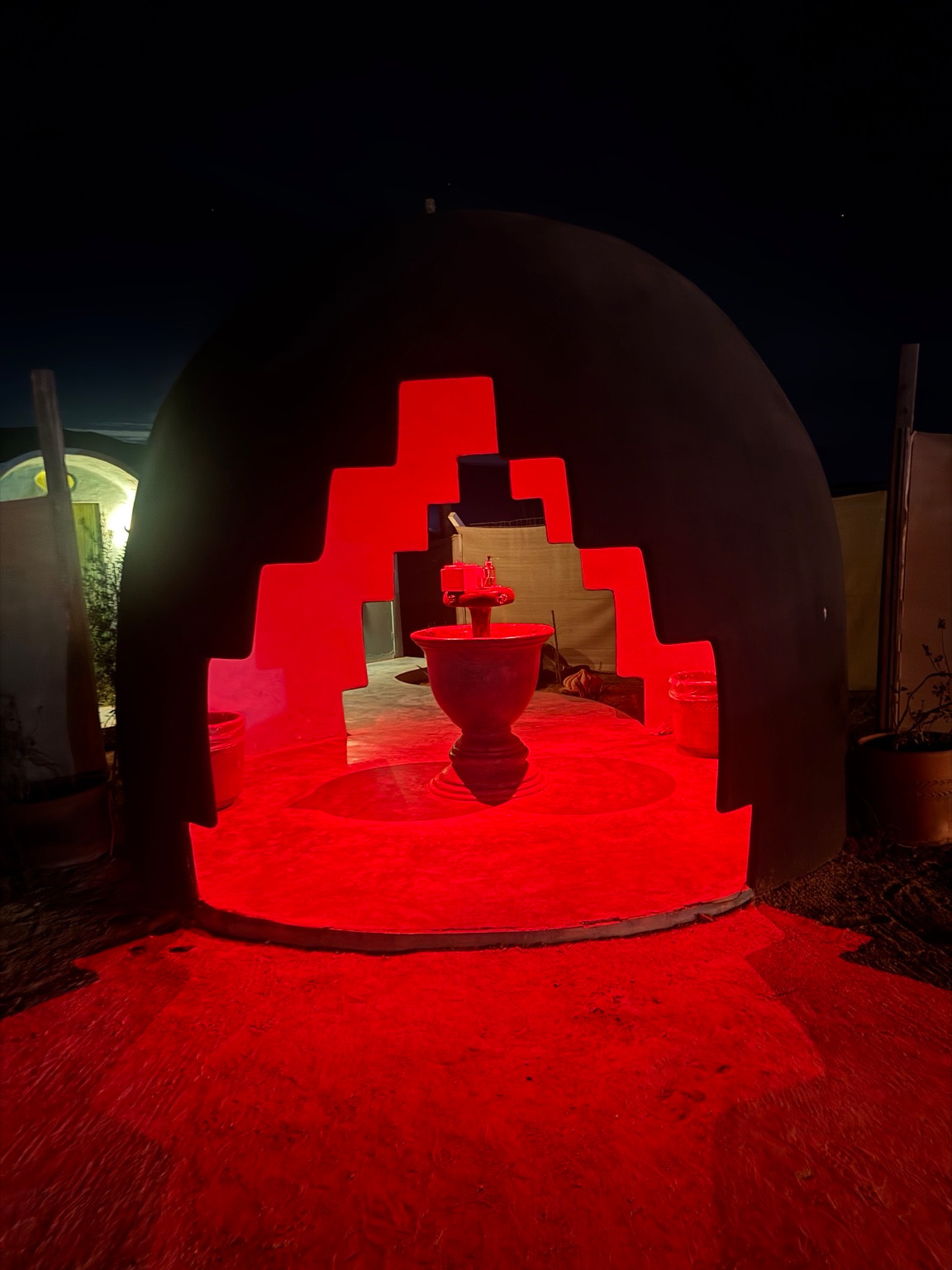 Red light illuminates a stepped arch and central fountain at Bloodlust Winebar at night.