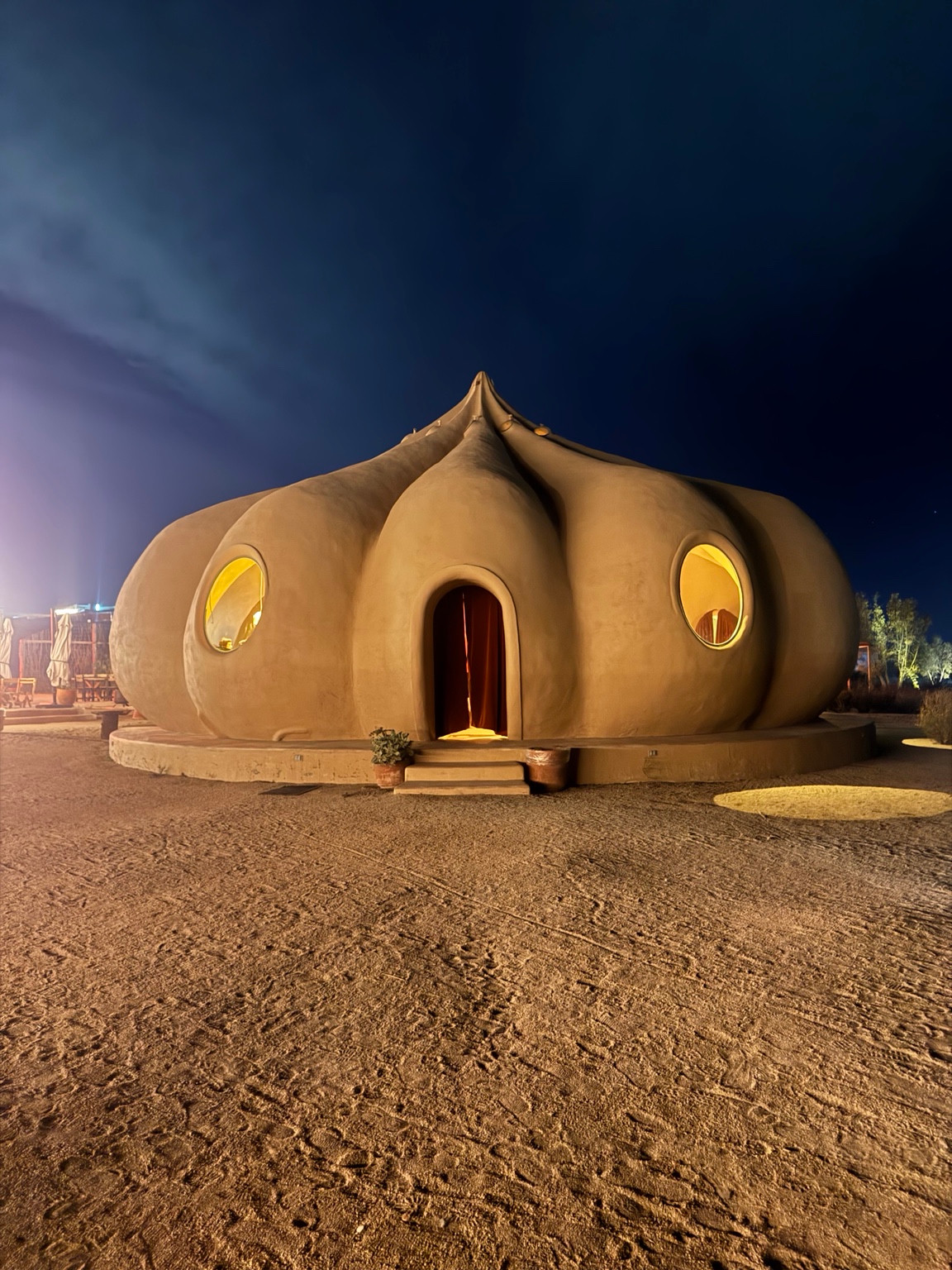 Rounded sculptural building at Bloodlust Winebar with glowing yellow windows beneath a dark blue sky.