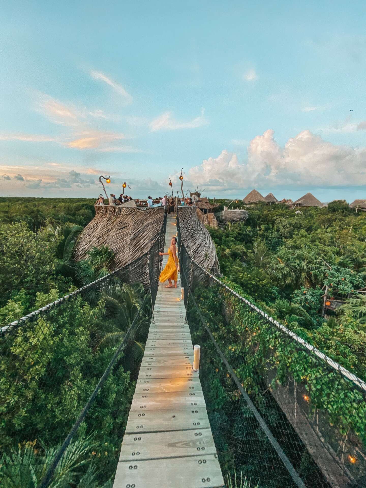 Giselle Lelux in a yellow dress on a tropical treetop bridge