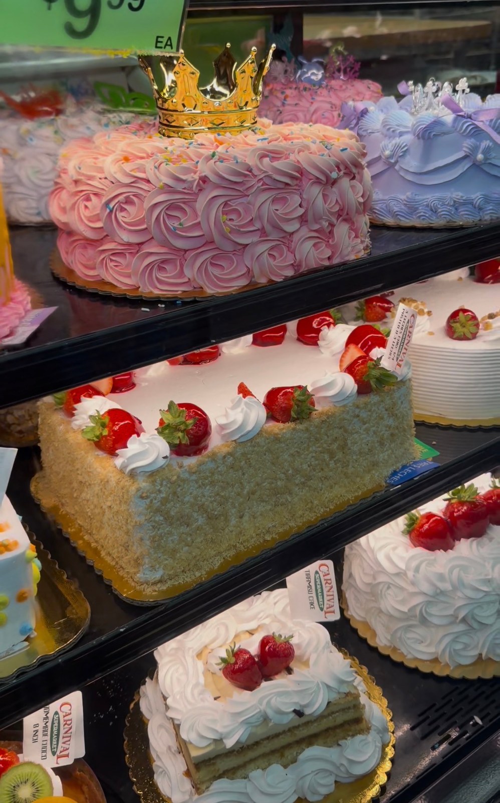 Pink and purple celebration cakes and strawberry-topped cakes in the Carnival National City bakery case.