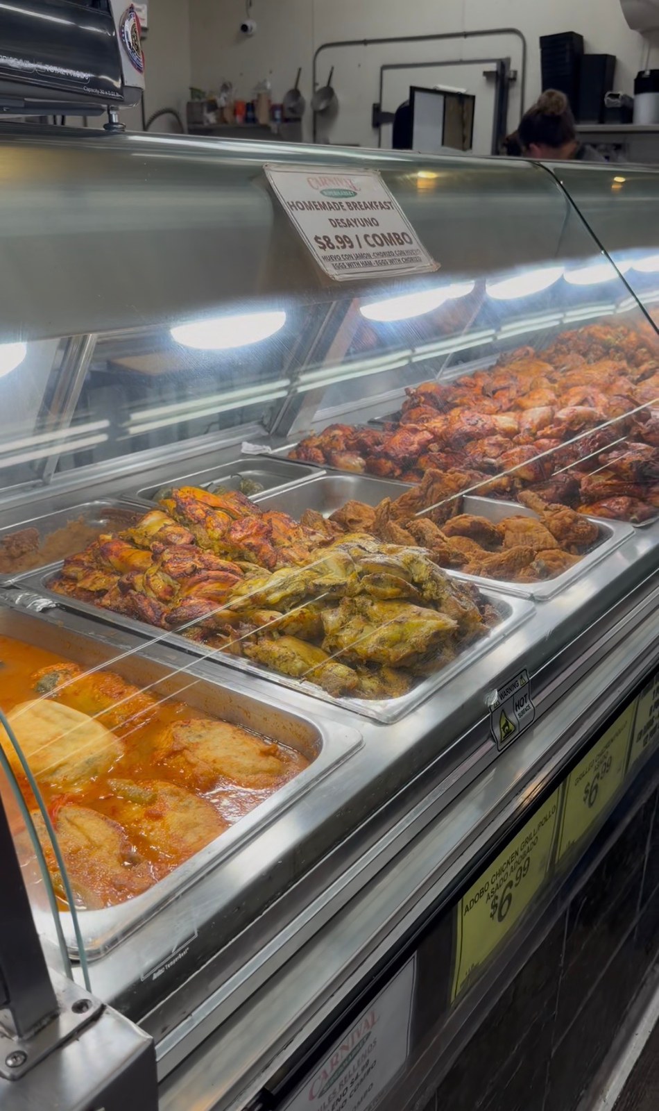 Trays of prepared chicken and other hot foods behind the glass counter at Carnival National City.