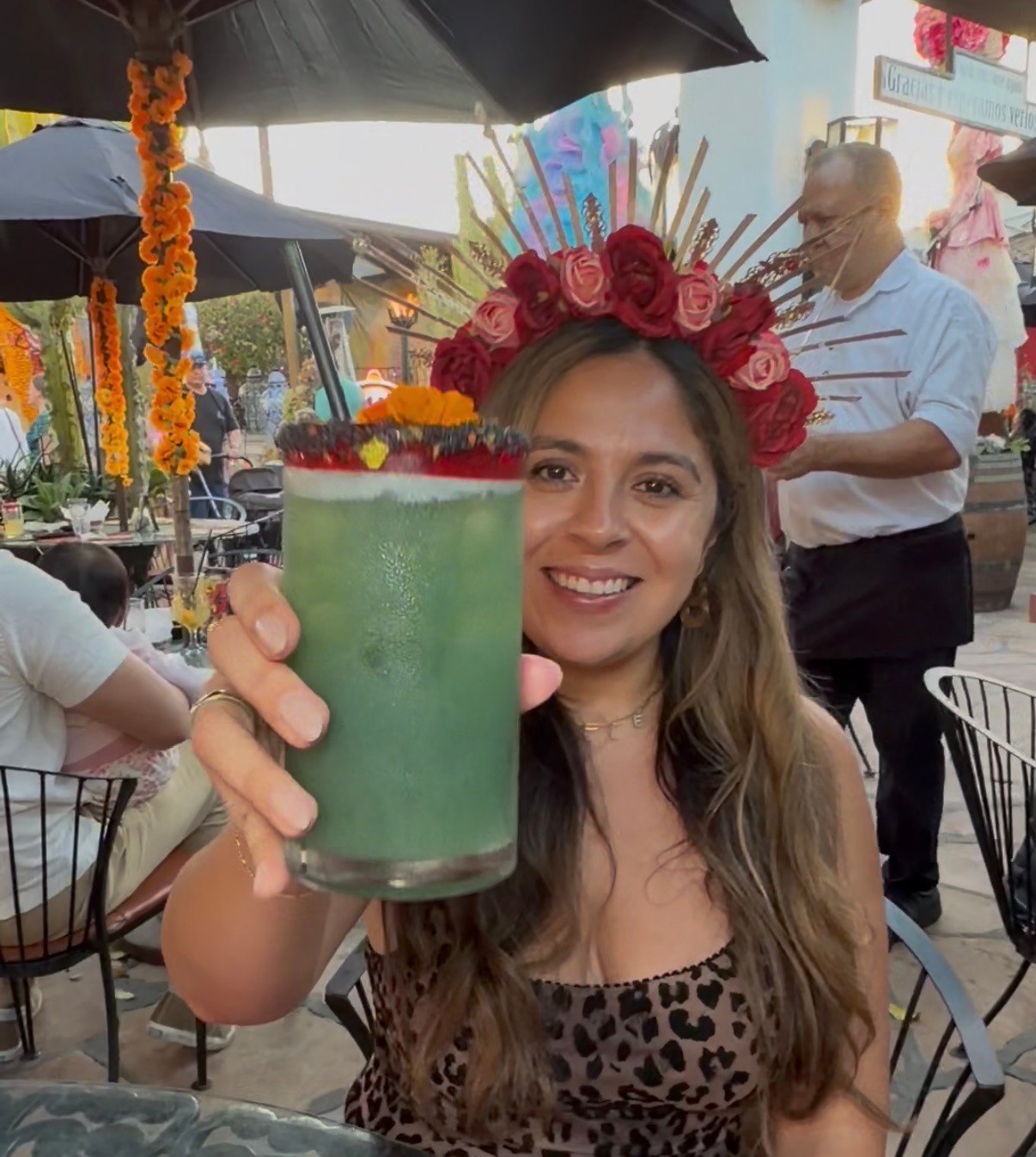 A woman in a pink flower crown holds a green drink in the decorated outdoor courtyard at Casa de Reyes.