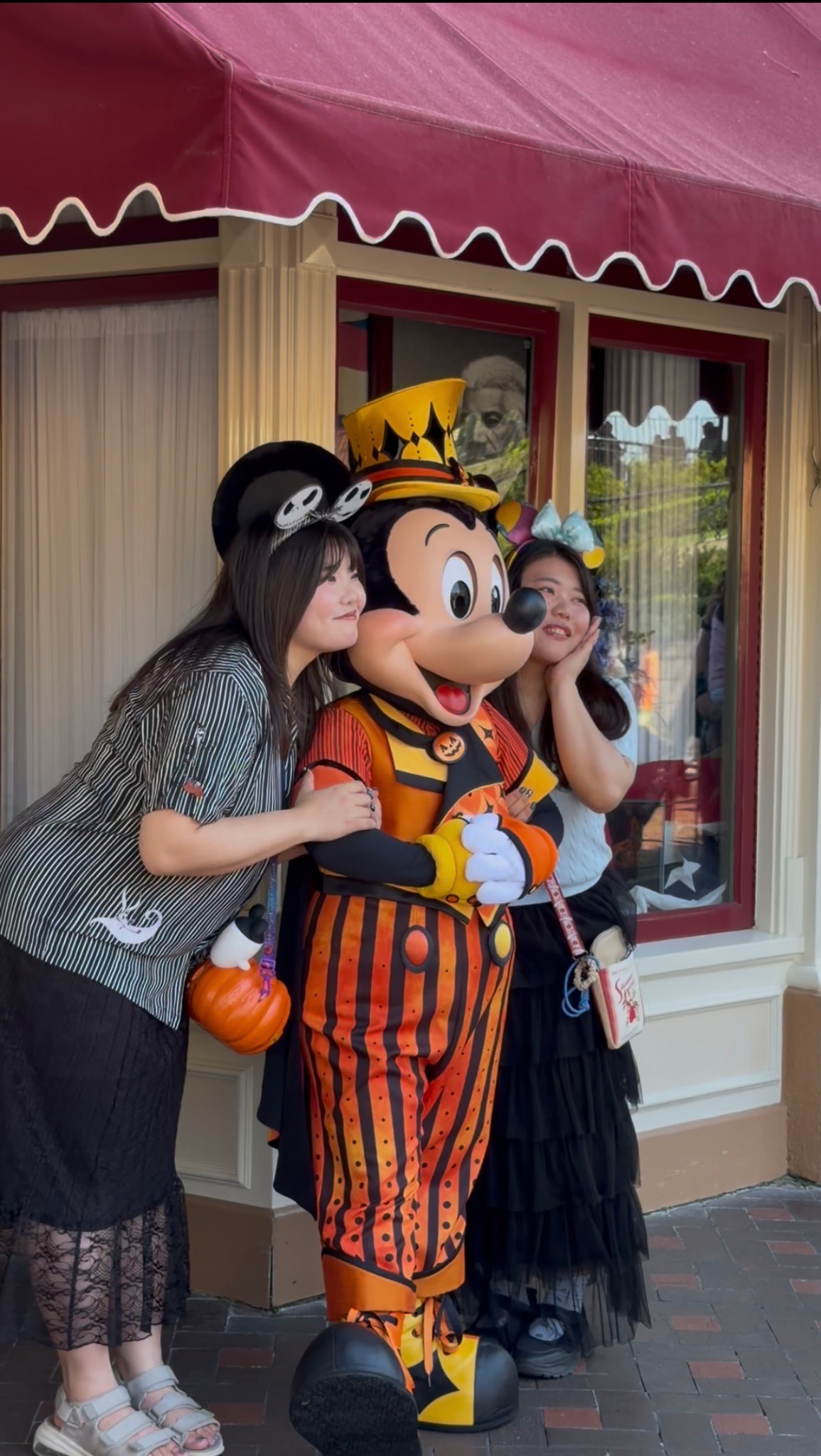 Two visitors posing with Mickey Mouse in an orange-and-black Halloween suit and top hat.