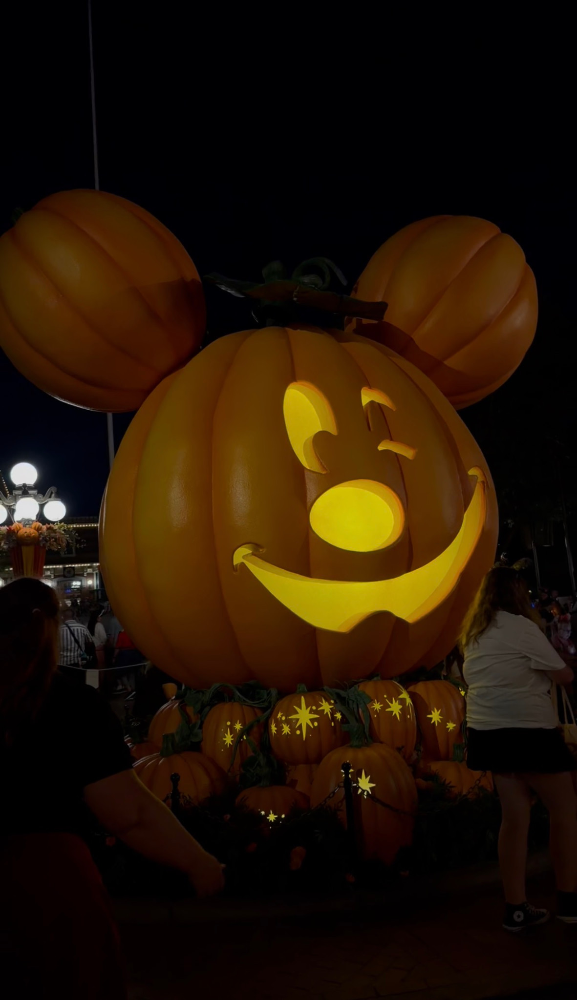An illuminated Mickey-shaped jack-o’-lantern above smaller pumpkins at night.