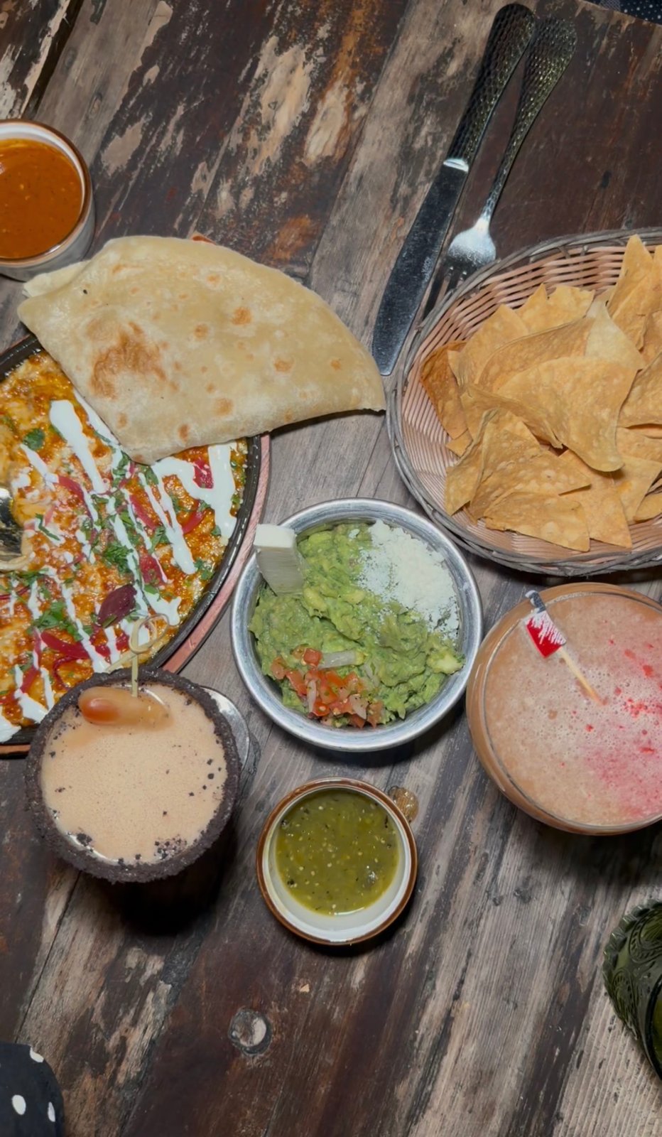 Tortilla chips, guacamole, a skillet dish, salsa and two cocktails on a wooden table at El Sueño.