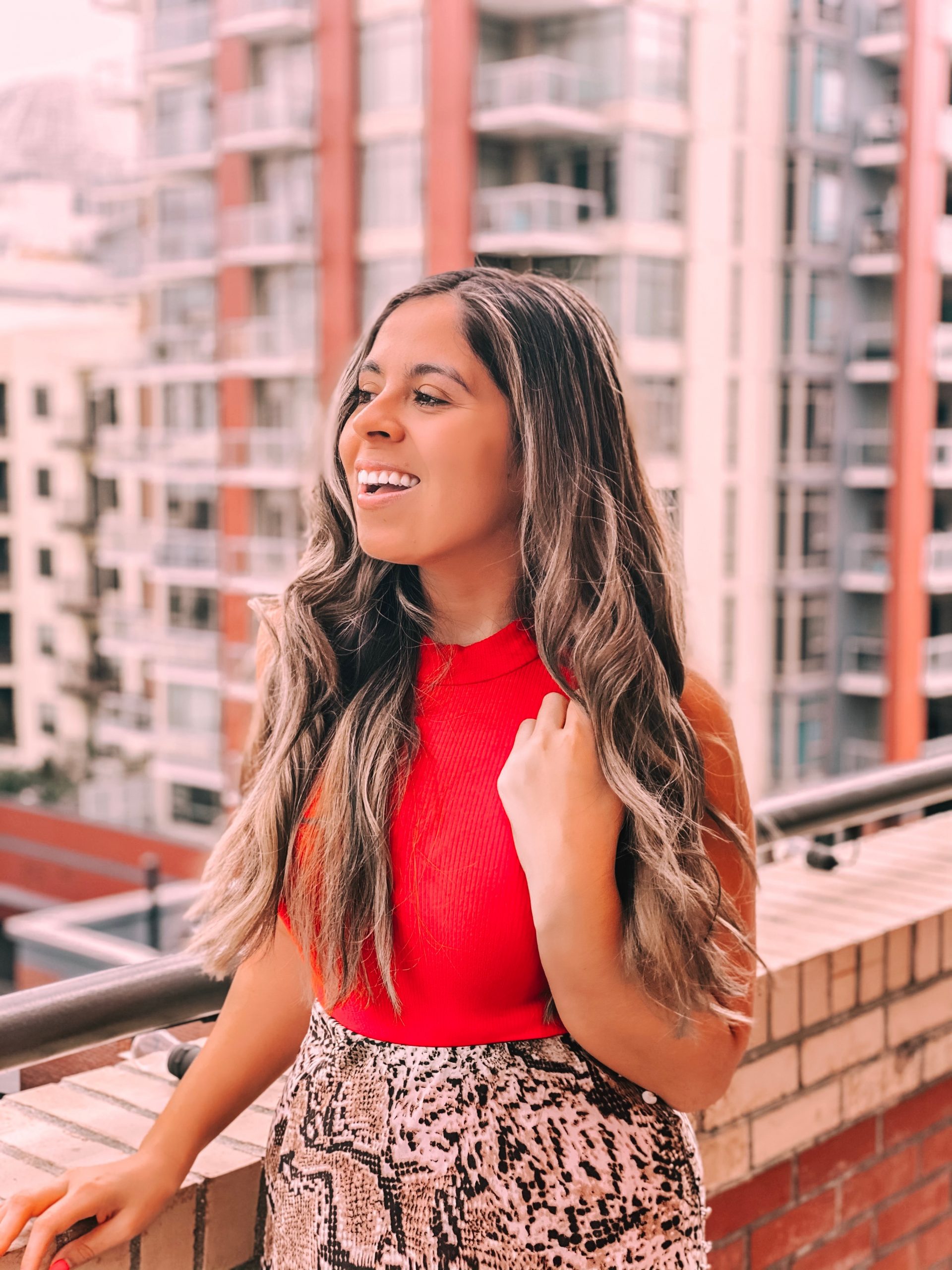 Giselle Lelux wearing a red top on a city balcony