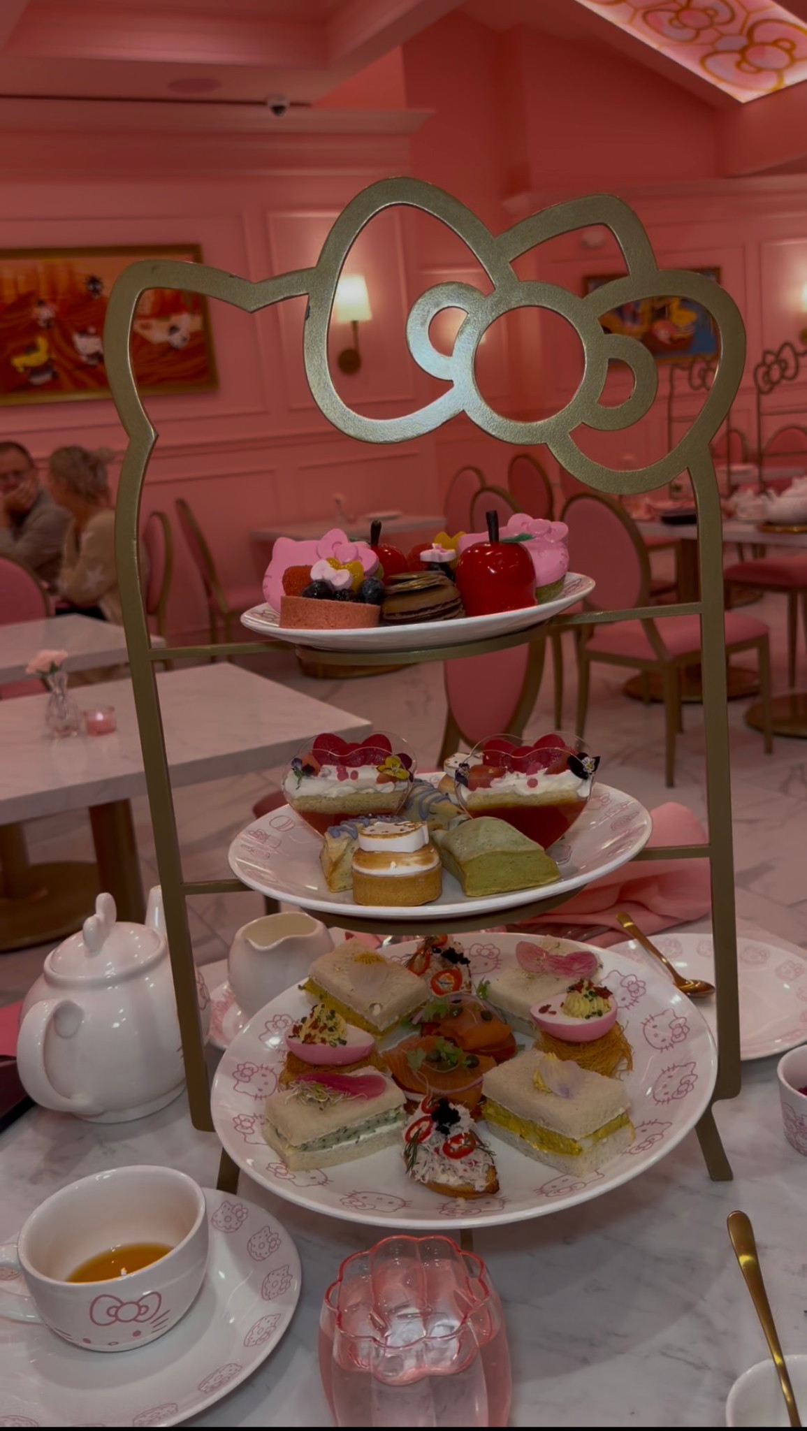 A three-tier afternoon tea stand shaped like Hello Kitty, with sweets and small sandwiches.