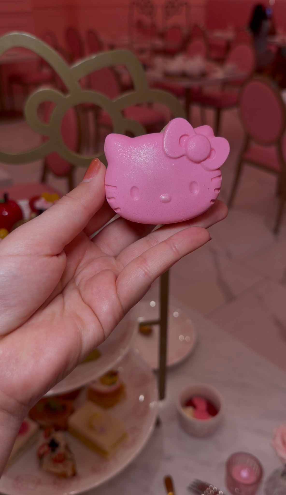 A hand holding a pink Hello Kitty-shaped treat in the pink tea room.