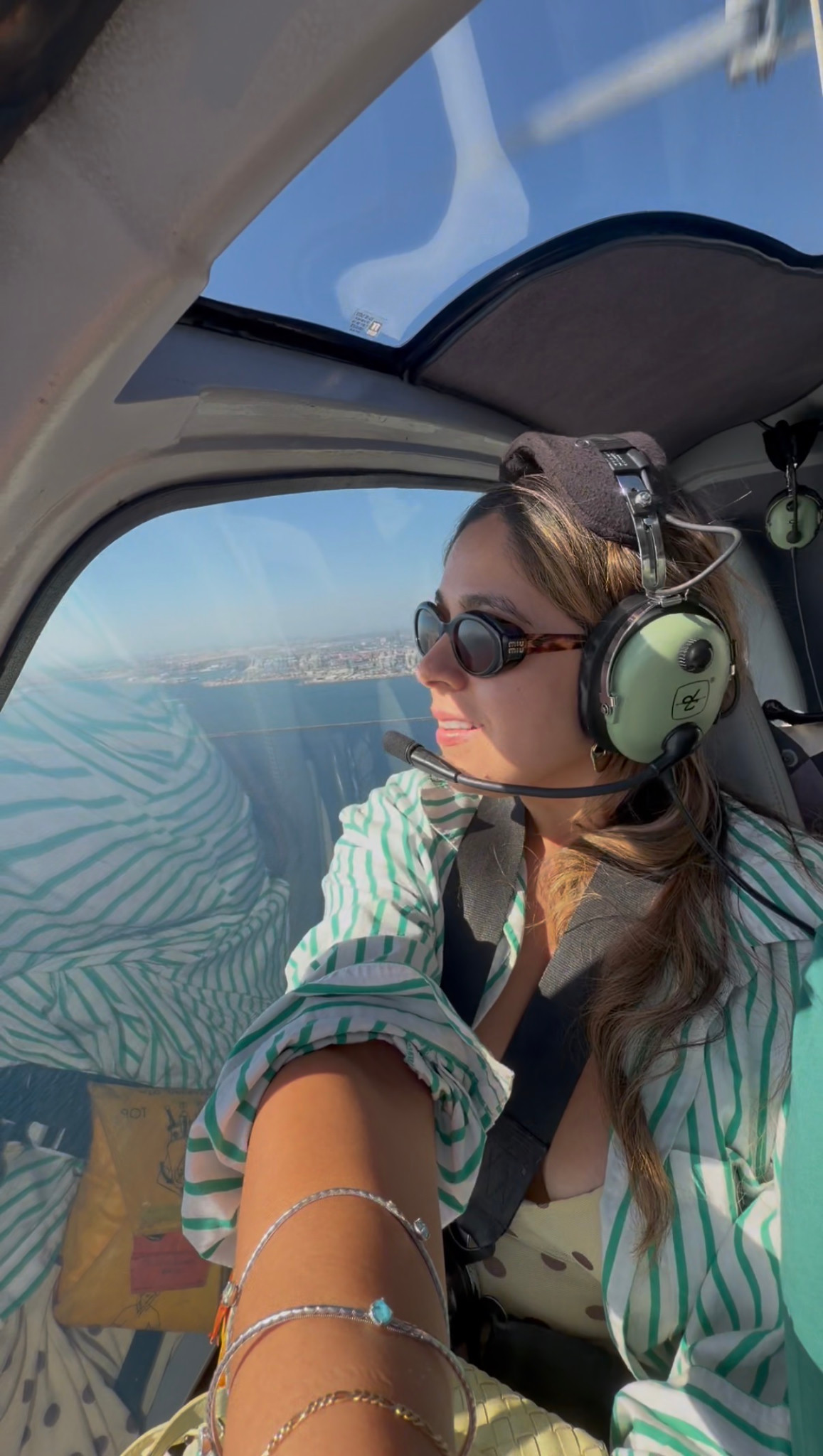 Giselle wearing a headset aboard a helicopter with the coastline visible through the window.