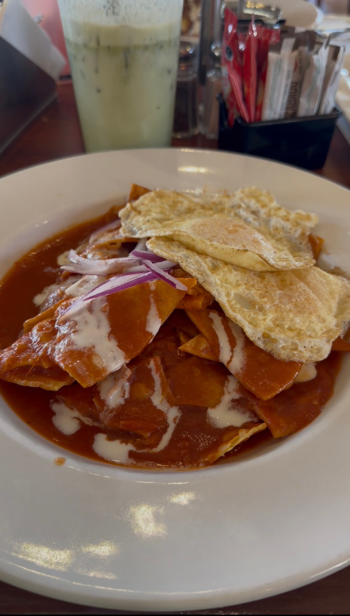 A plate of chilaquiles topped with fried eggs, with an iced green drink behind it.