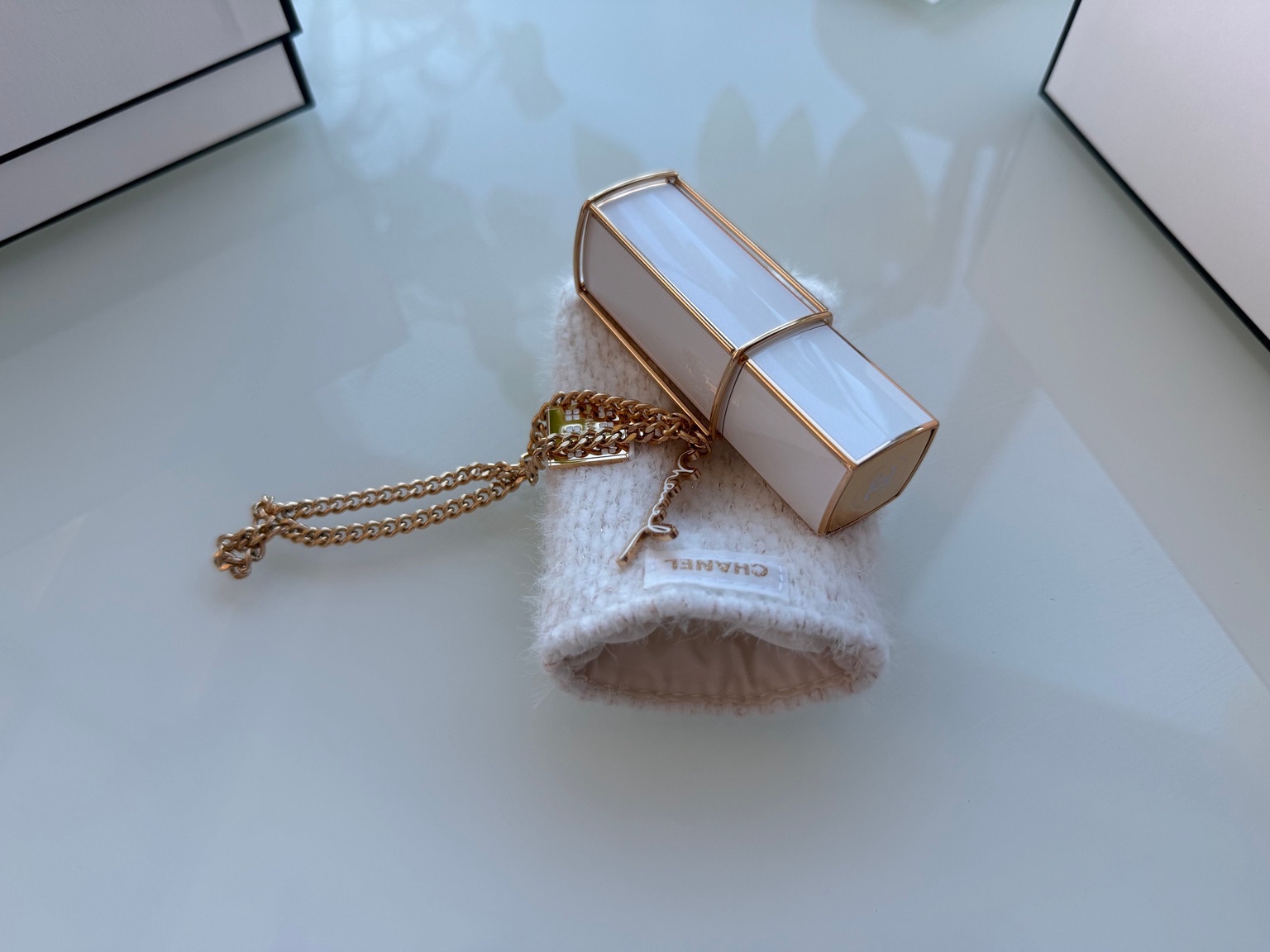 Cream and gold Chanel purse spray resting on a white woven sleeve with a gold-tone charm chain.