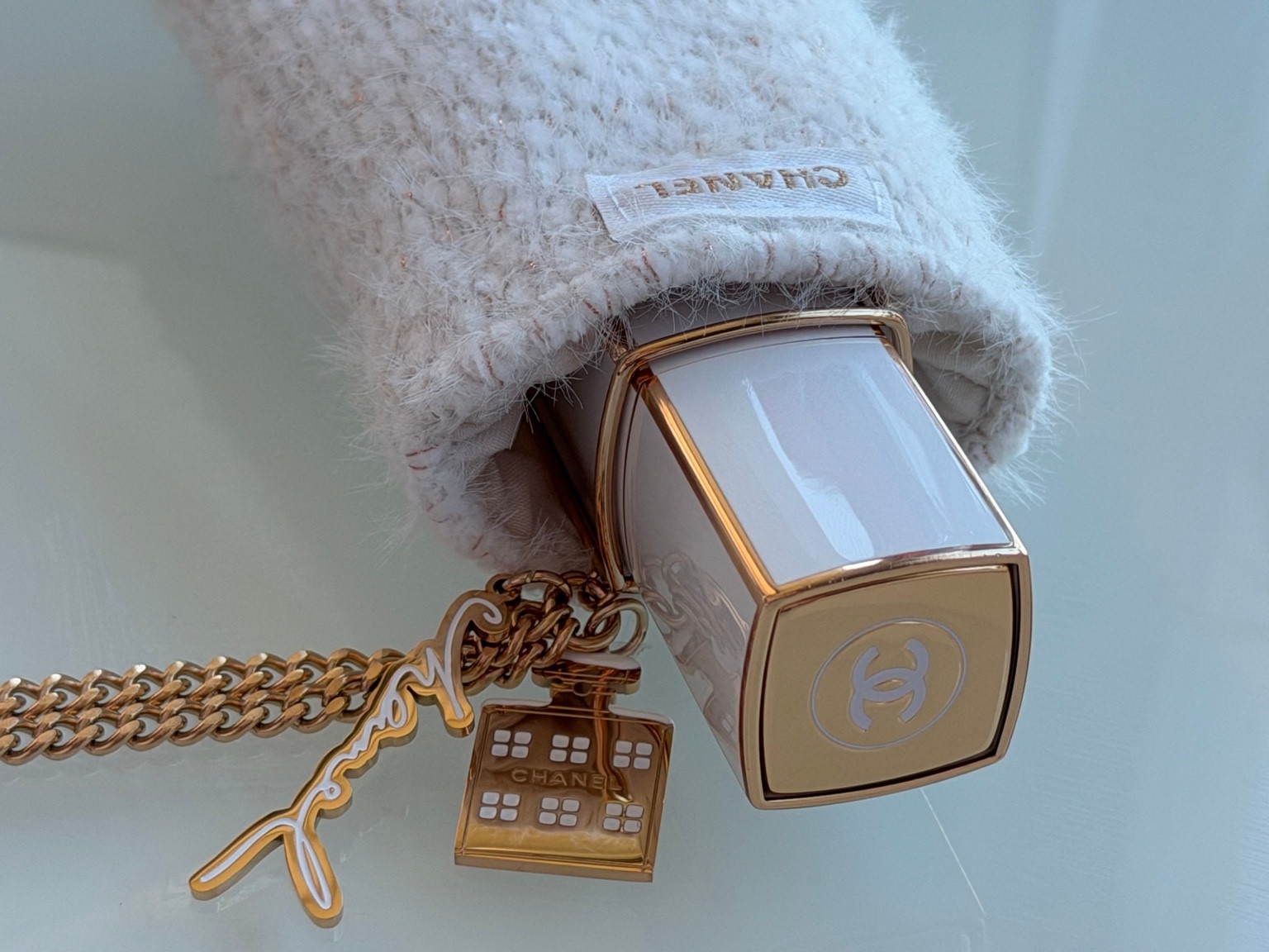 Close-up of a cream Chanel purse-spray case, woven sleeve and gold-tone bottle and signature charms.