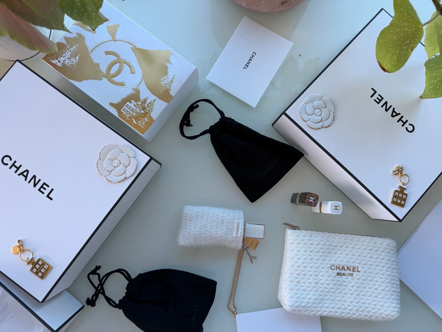Overhead view of Chanel white boxes, camellias, gold charms, knit pouches and small beauty items.