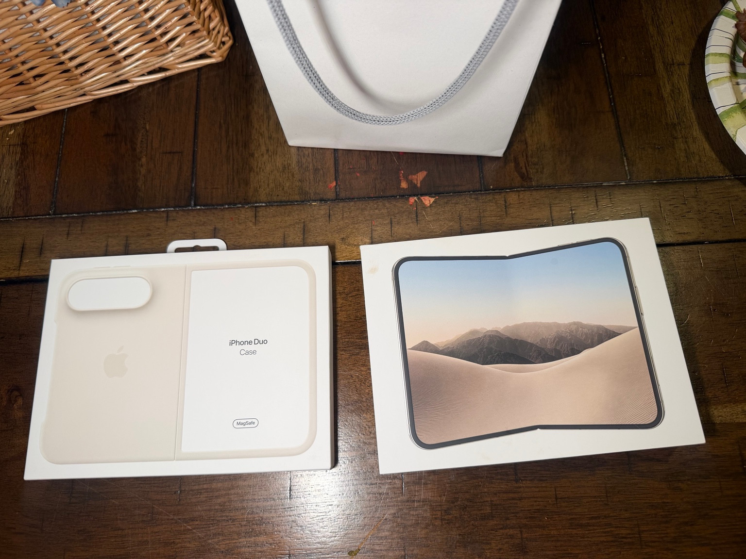 An iPhone Duo box and separate iPhone Duo case box on a wooden table beneath a white shopping bag.