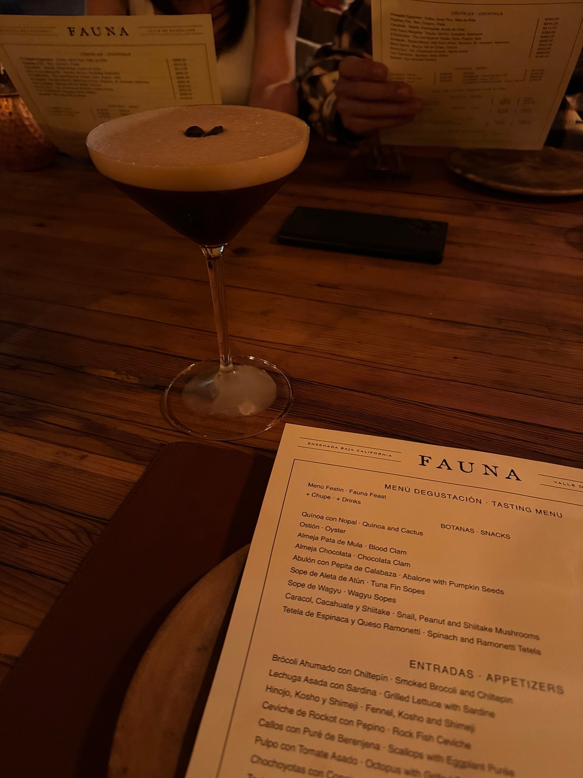 A foamy cocktail and Fauna menus on a wooden dining table.