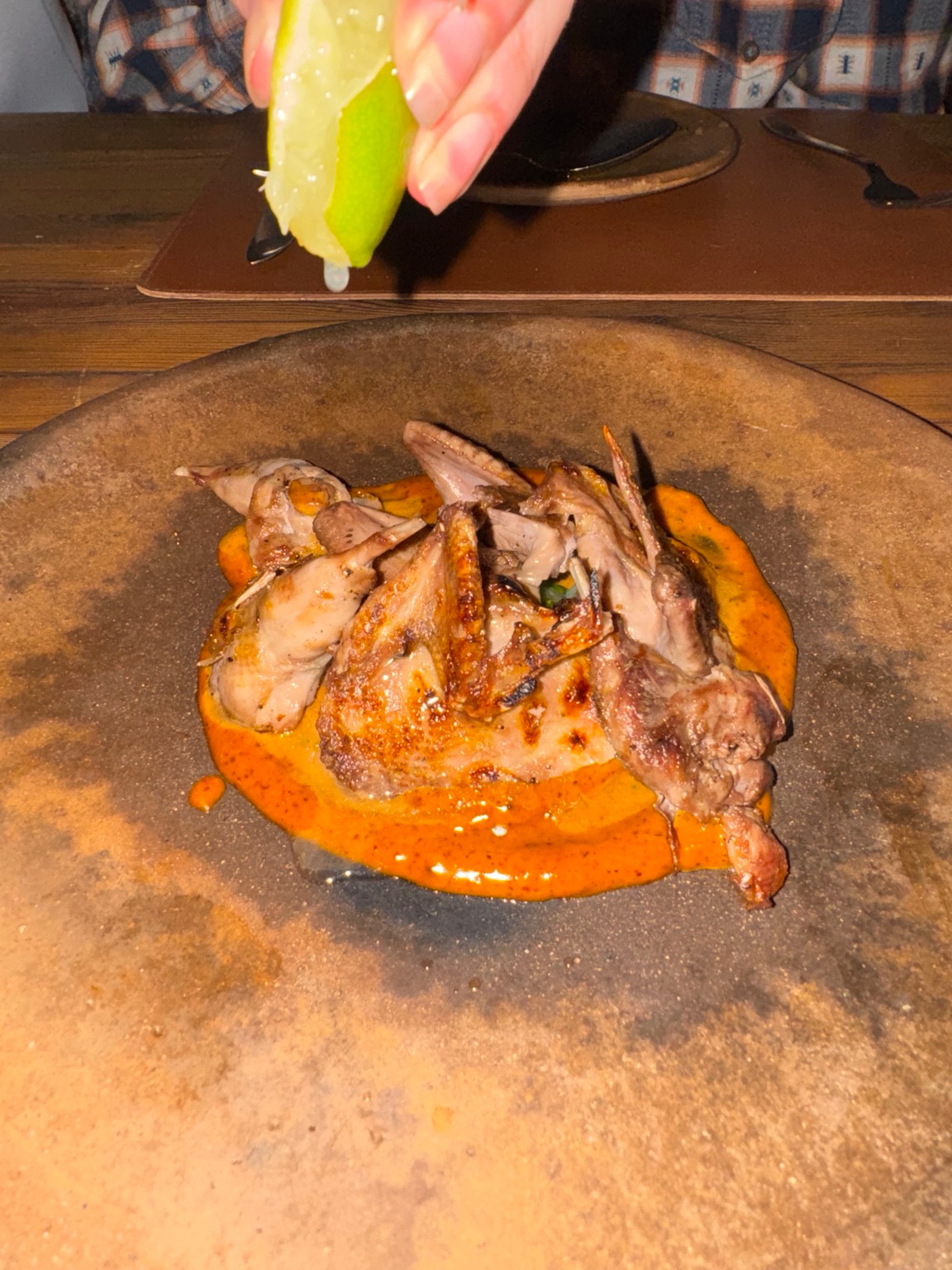 A plated dish with orange sauce as a hand squeezes a lime above it at Fauna.
