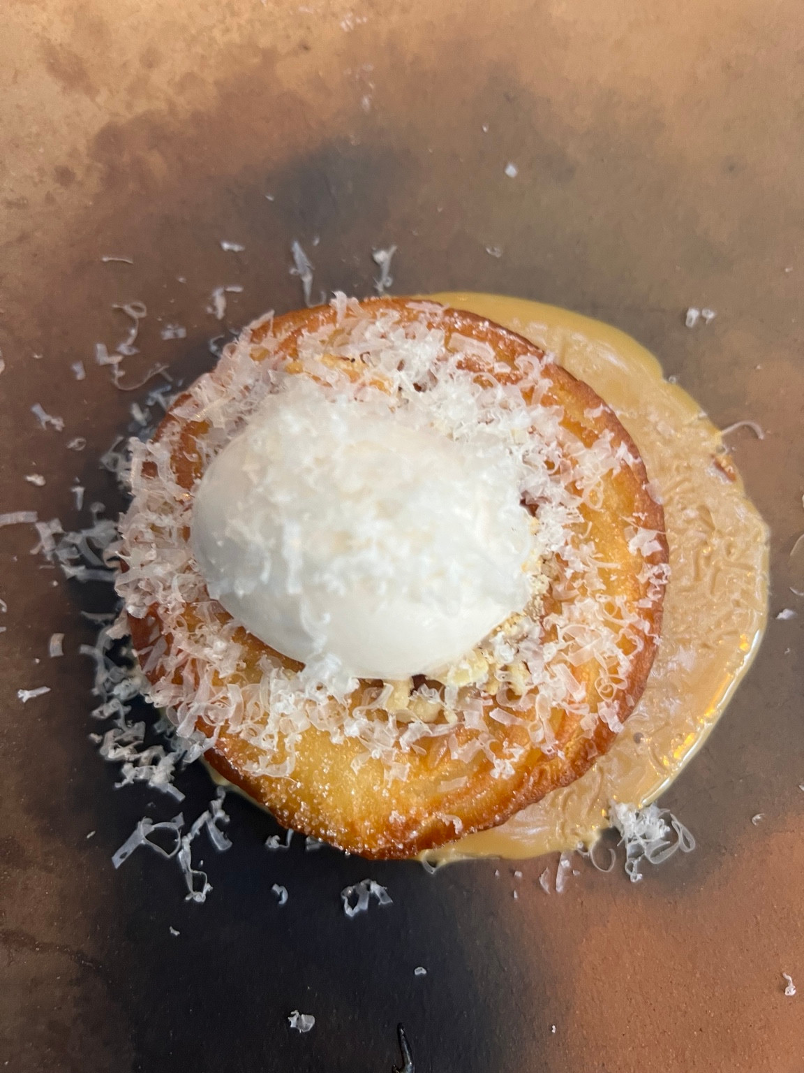 A round golden dish with a white scoop and fine shavings on a brown plate at Fauna.