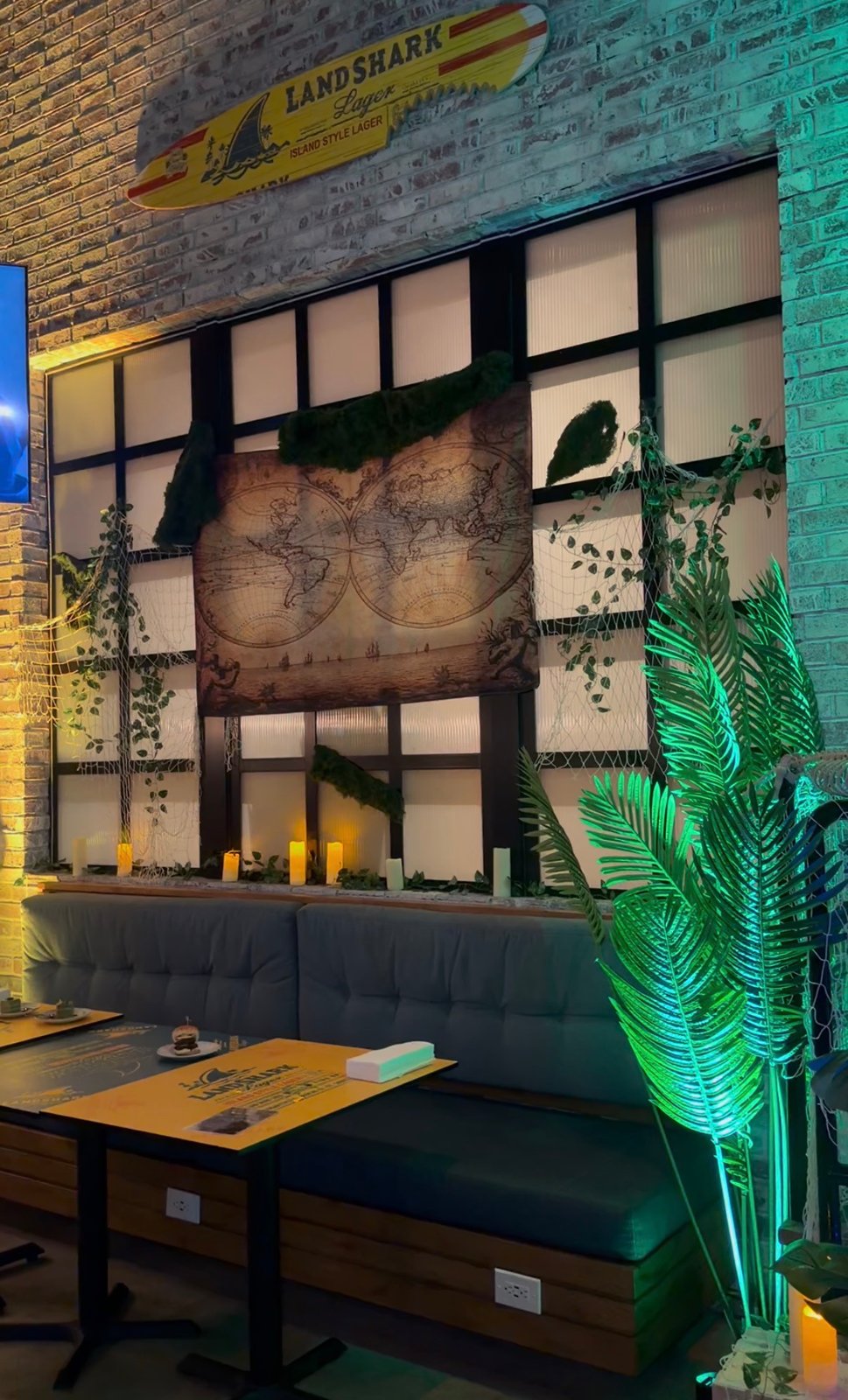A vintage-style world map, draped netting, vines and candles above booth seating at Lost Temple Tavern.