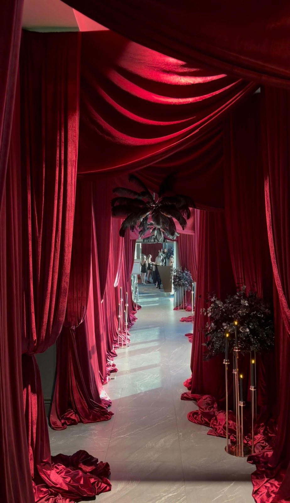 A corridor draped in red fabric with dark feather decorations at Masquerade After Dark.