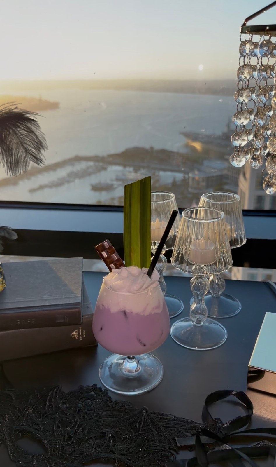A purple cocktail topped with whipped cream and a chocolate bar beside a window overlooking San Diego Bay.