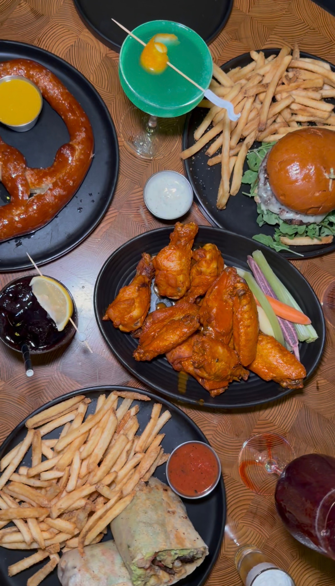 Overhead view of a pretzel, chicken wings, burger, wrap, fries and colorful drinks at Nason's Beer Hall.