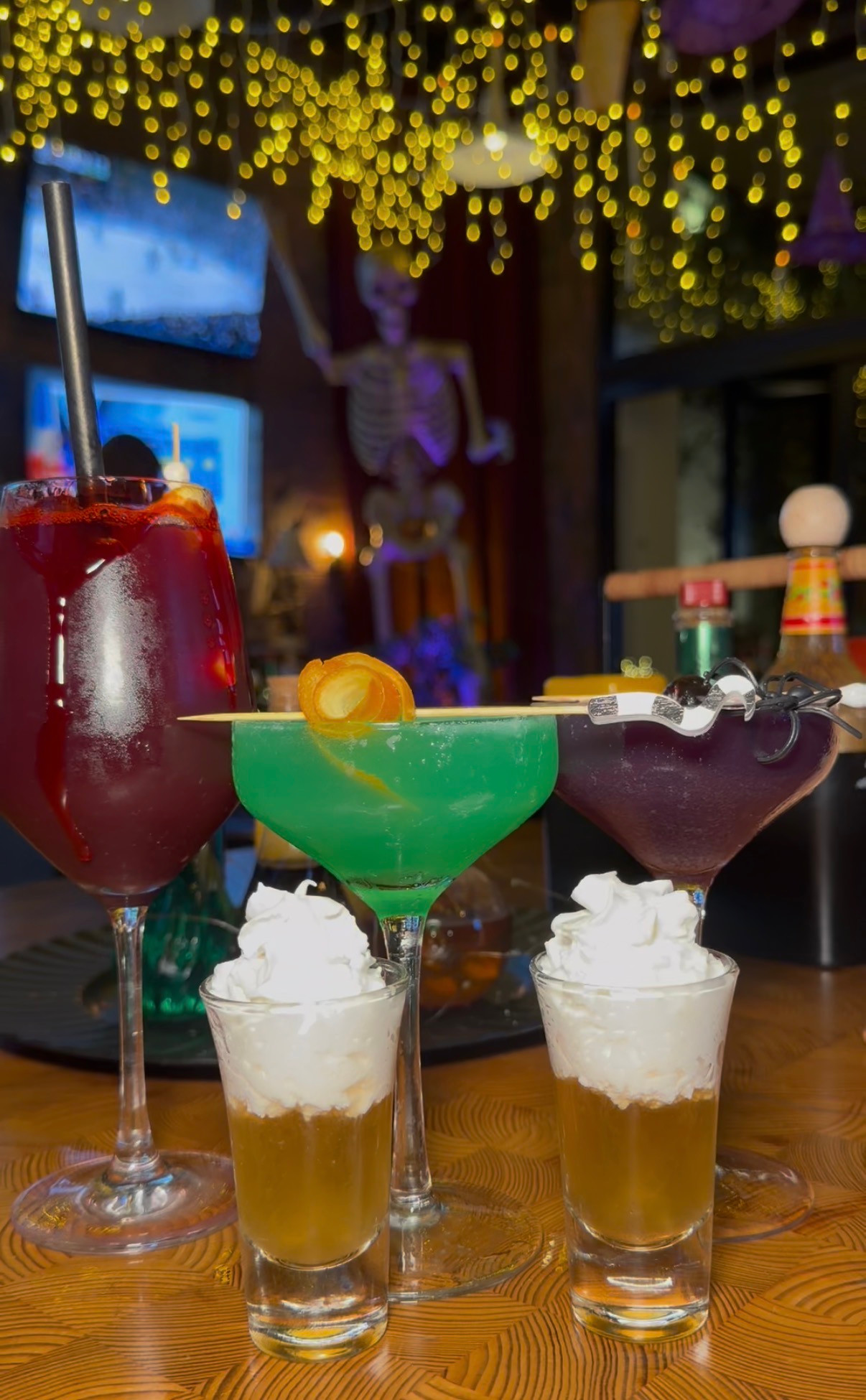 Red, green and purple drinks with two whipped-cream-topped shots beneath Halloween lights at Nason's Beer Hall.