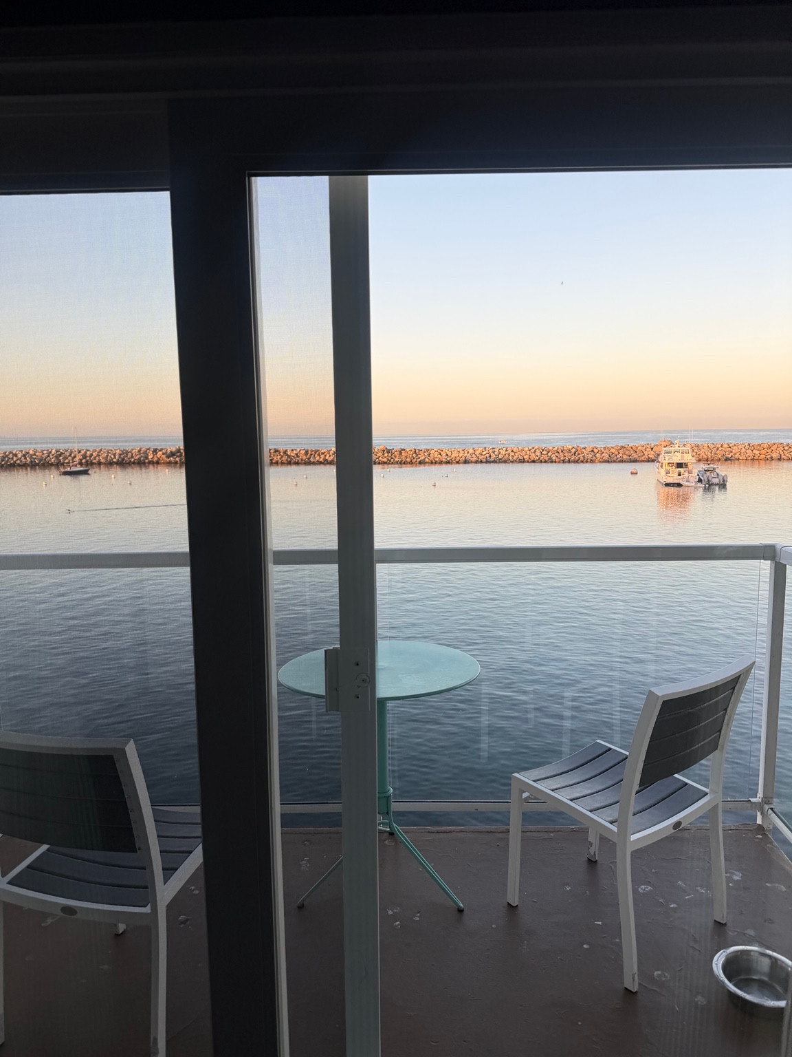 Two chairs and a glass table on a Portofino balcony overlooking boats and the harbor breakwater.