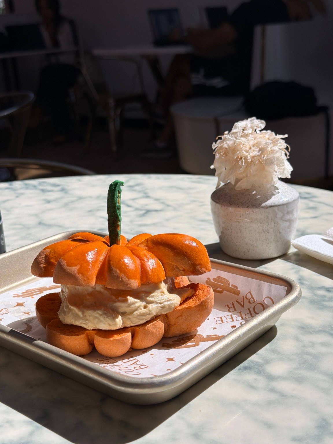 Orange pumpkin-shaped bagel with a thick cream cheese filling on an S3 Coffee Bar tray.