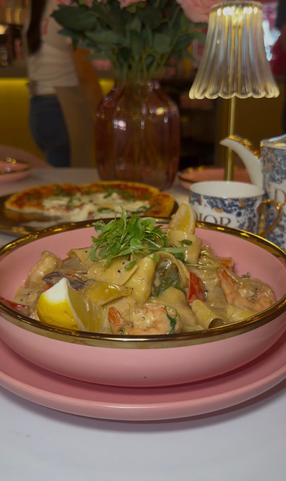 Pasta with shrimp, greens and lemon wedges served in a pink bowl at Saya Brasserie.