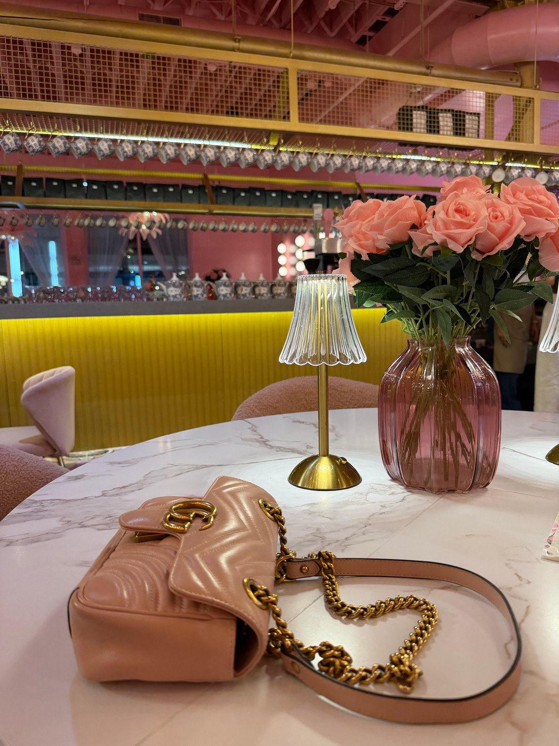 Pink roses, a gold table lamp and a pink handbag on a marble-patterned table inside Saya Brasserie.