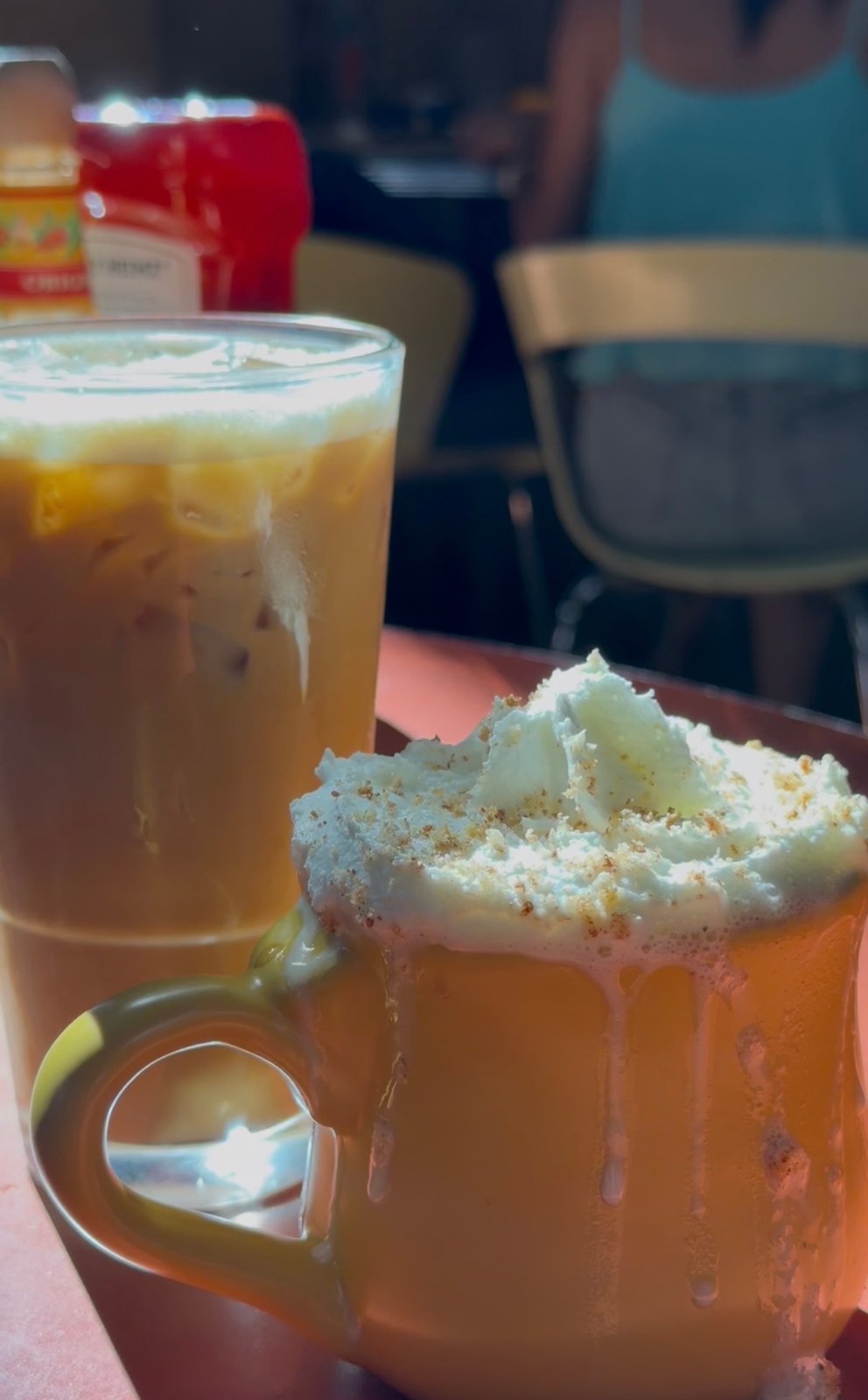 An iced coffee beside a hot drink topped with whipped cream in an orange mug at Snooze.