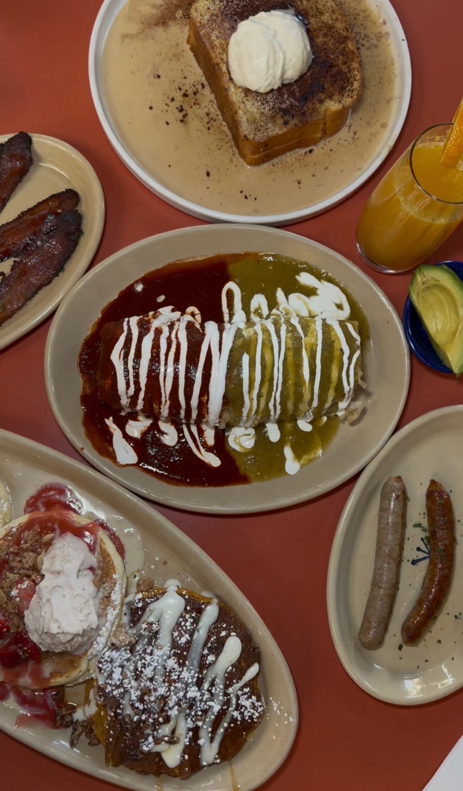 An overhead view of a Snooze brunch spread with a pancake flight, French toast, a sauce-covered burrito and breakfast sides.
