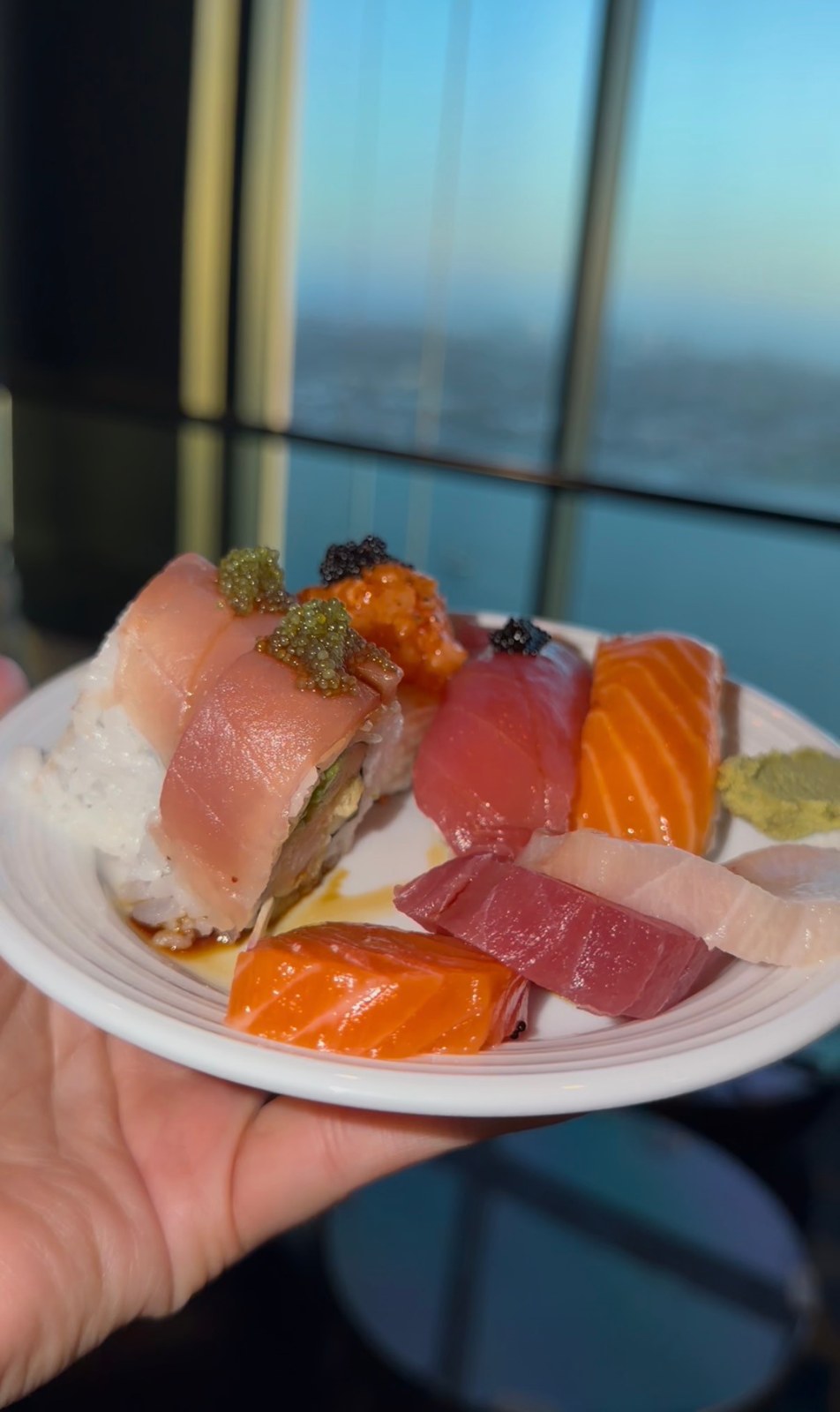 A plate of sushi rolls, nigiri and sashimi held in front of the windows at Top of the Hyatt.