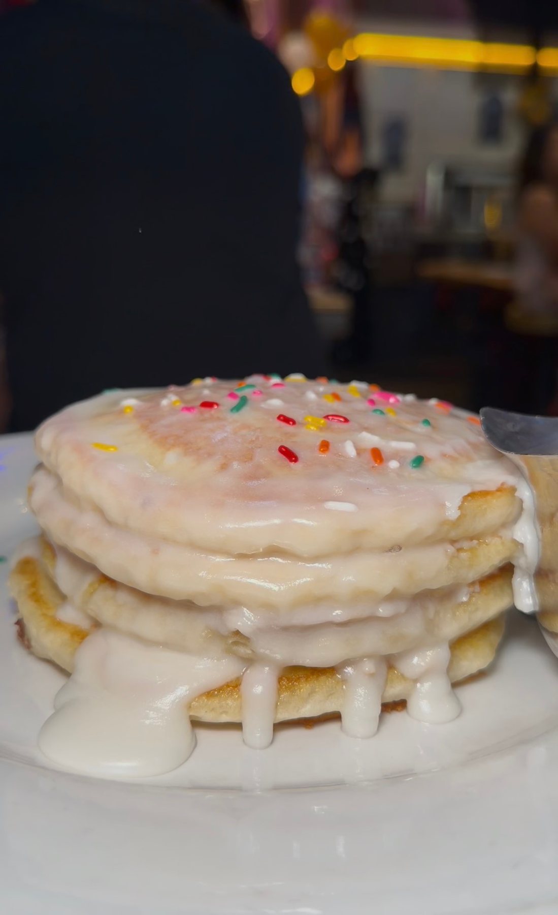 A stack of Werewolf doughnut pancakes covered in white icing and colorful sprinkles.