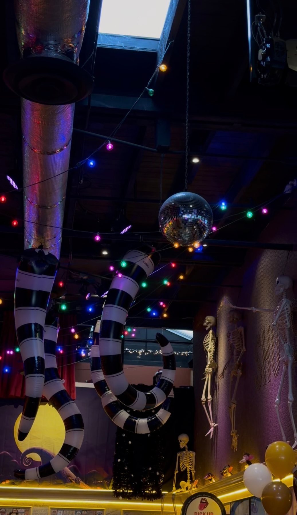 Black-and-white striped Halloween decorations and skeletons beneath colored string lights at Werewolf.