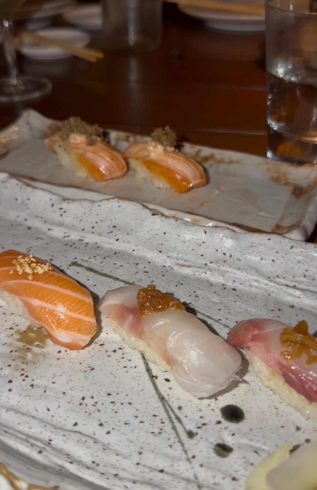 Assorted nigiri on ceramic plates, including salmon nigiri in the foreground and torched salmon behind.